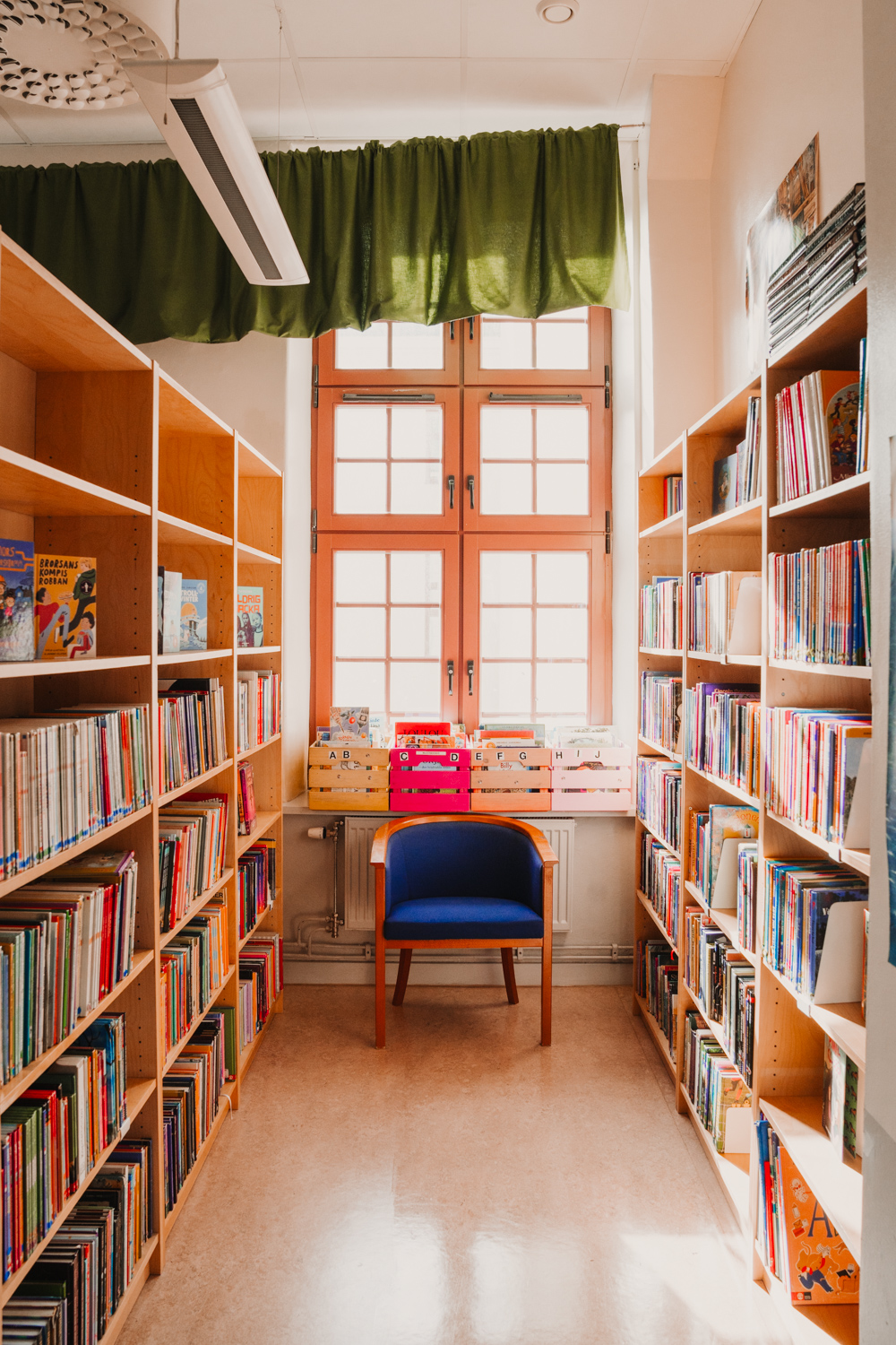 Två bokhyllor i ett bibliotek som står bredvid en blå fåtölj
