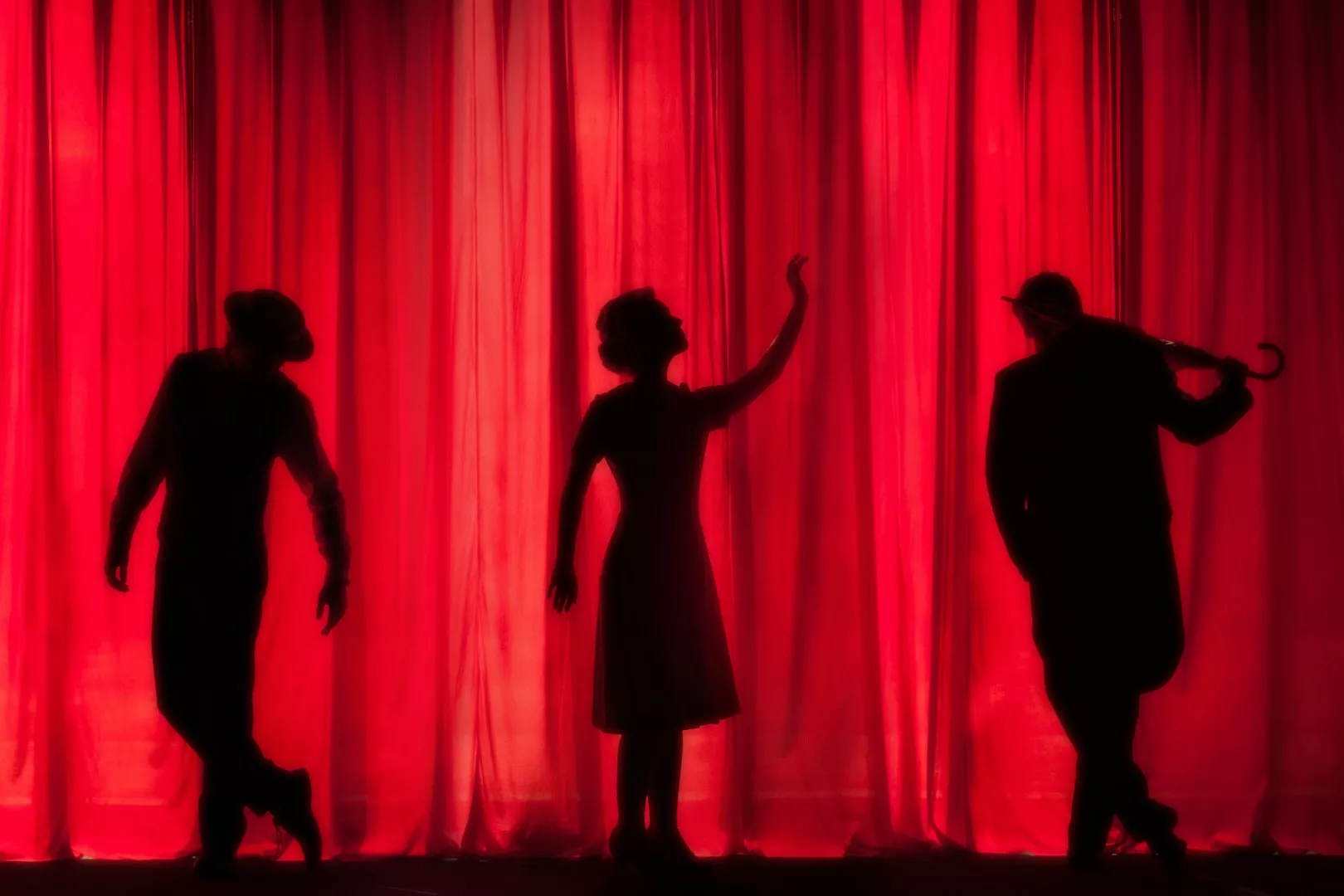 silhouettes of three people on a red curtain
